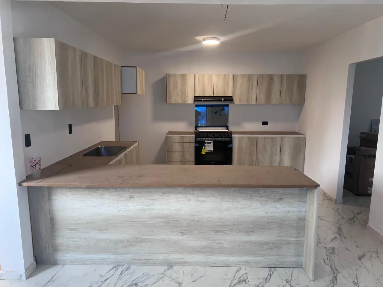 Cocina recién remodelada con carpintería de madera clara y barra en L