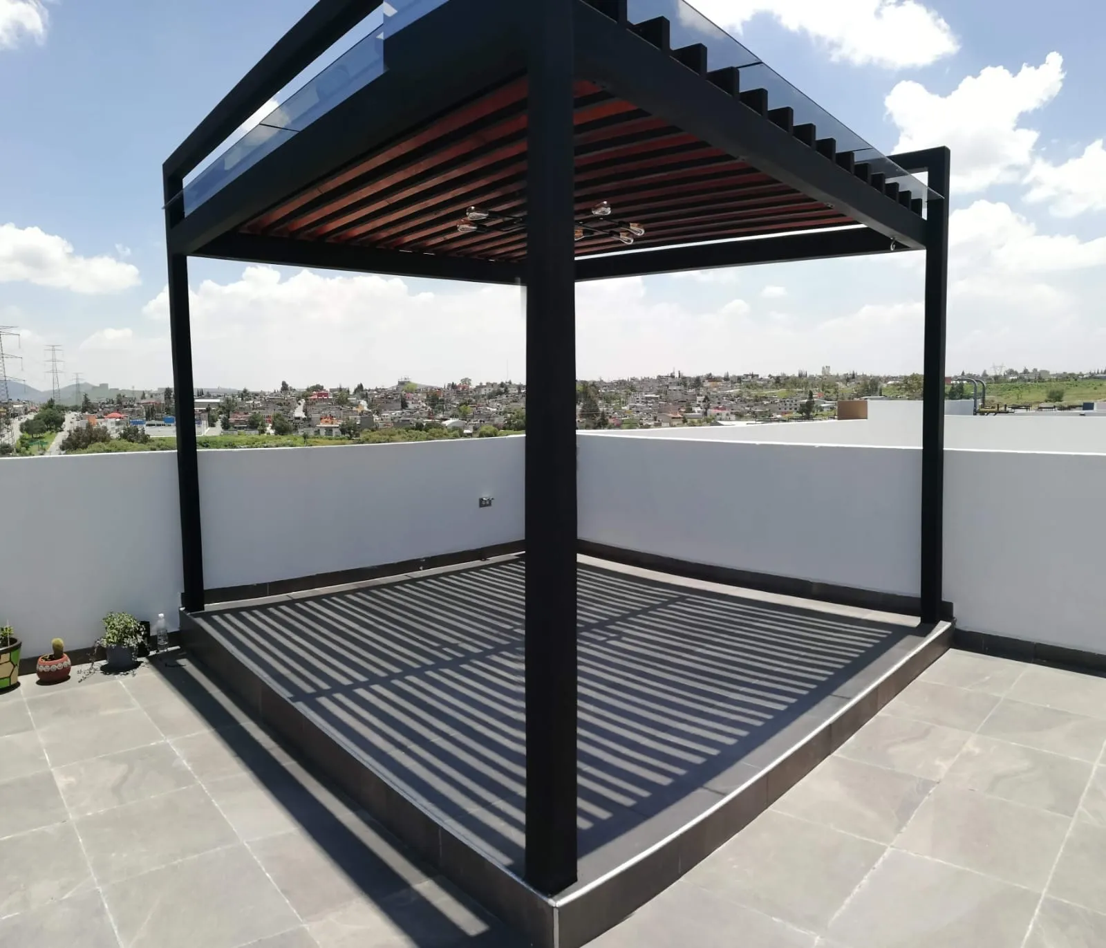 Pérgola de acero negro con cubierta de cristal en un roof garden al mediodía