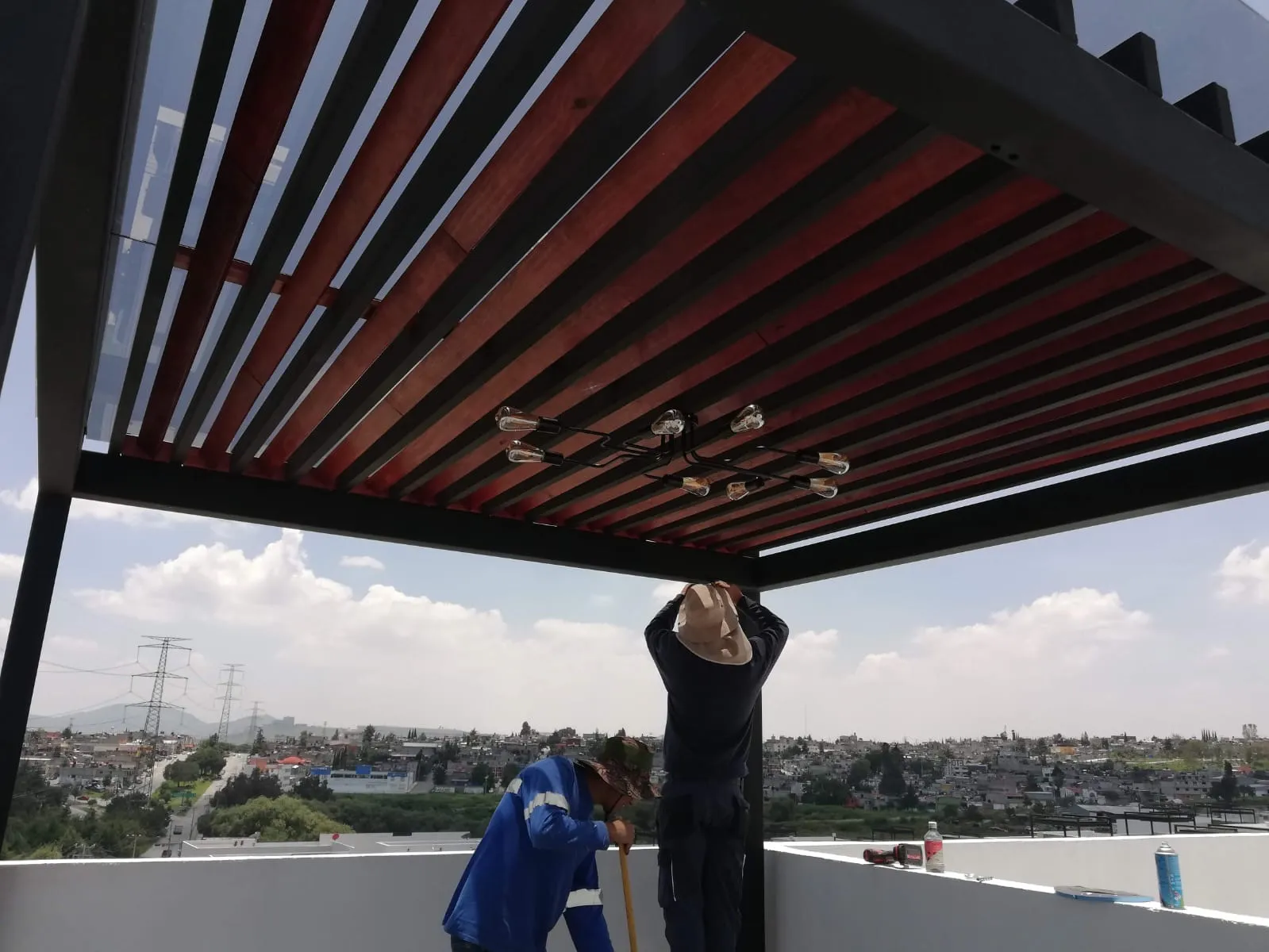 Vista inferior de pérgola con vigas de madera, cristal y lámpara vintage en terraza