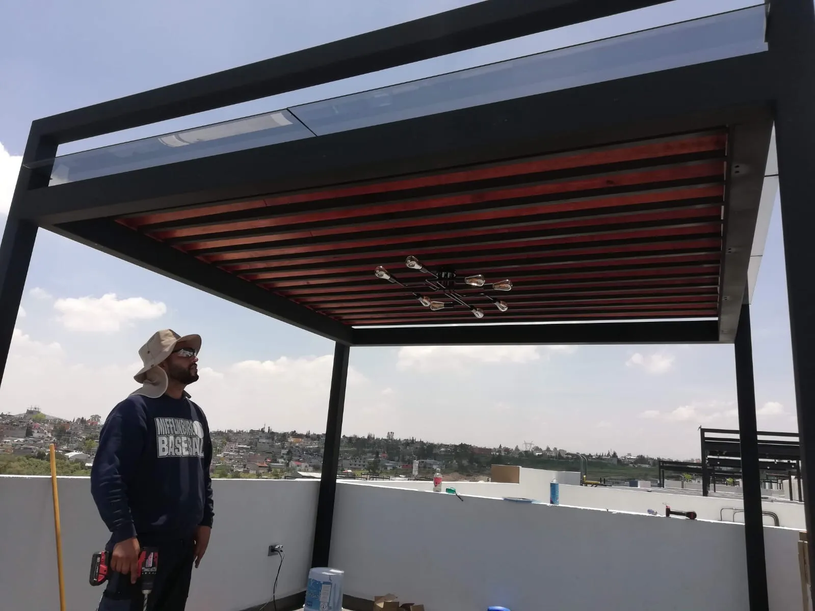 Instalador revisando pérgola de acero con celosía de madera y techo de cristal en azotea