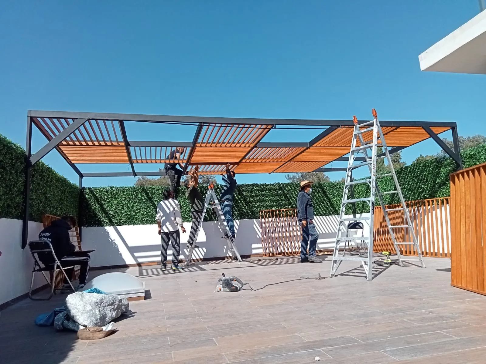 Cuadrilla instalando paneles de celosía de madera en pérgola metálica con muro verde