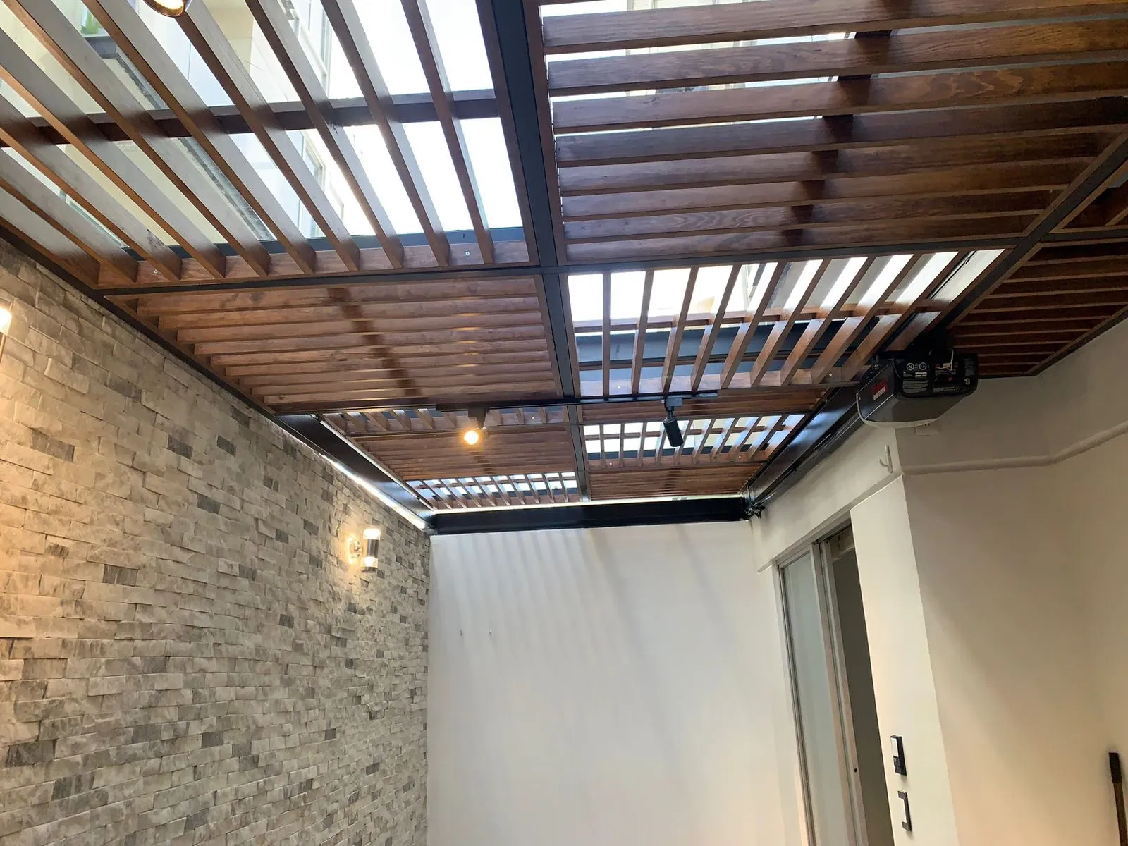 Pérgola de madera y acero con iluminación en patio con muro de piedra