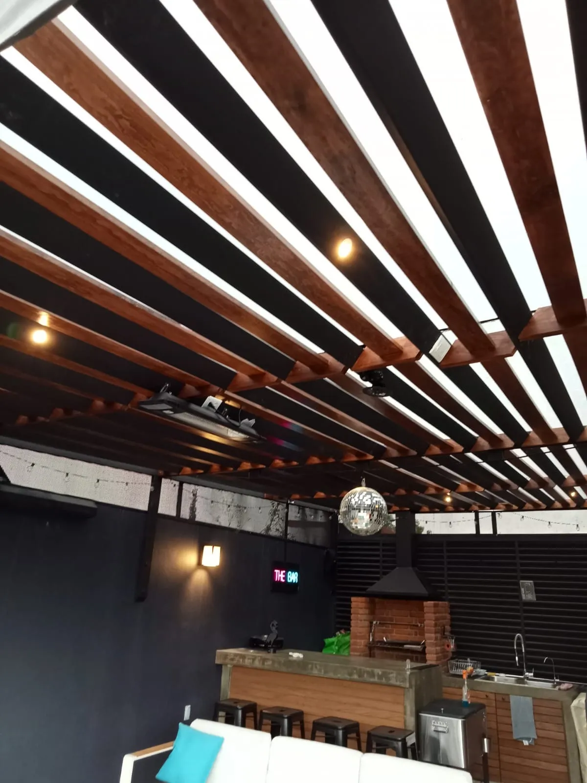 Pérgola de vigas de madera y acero negro con iluminación en bar de terraza