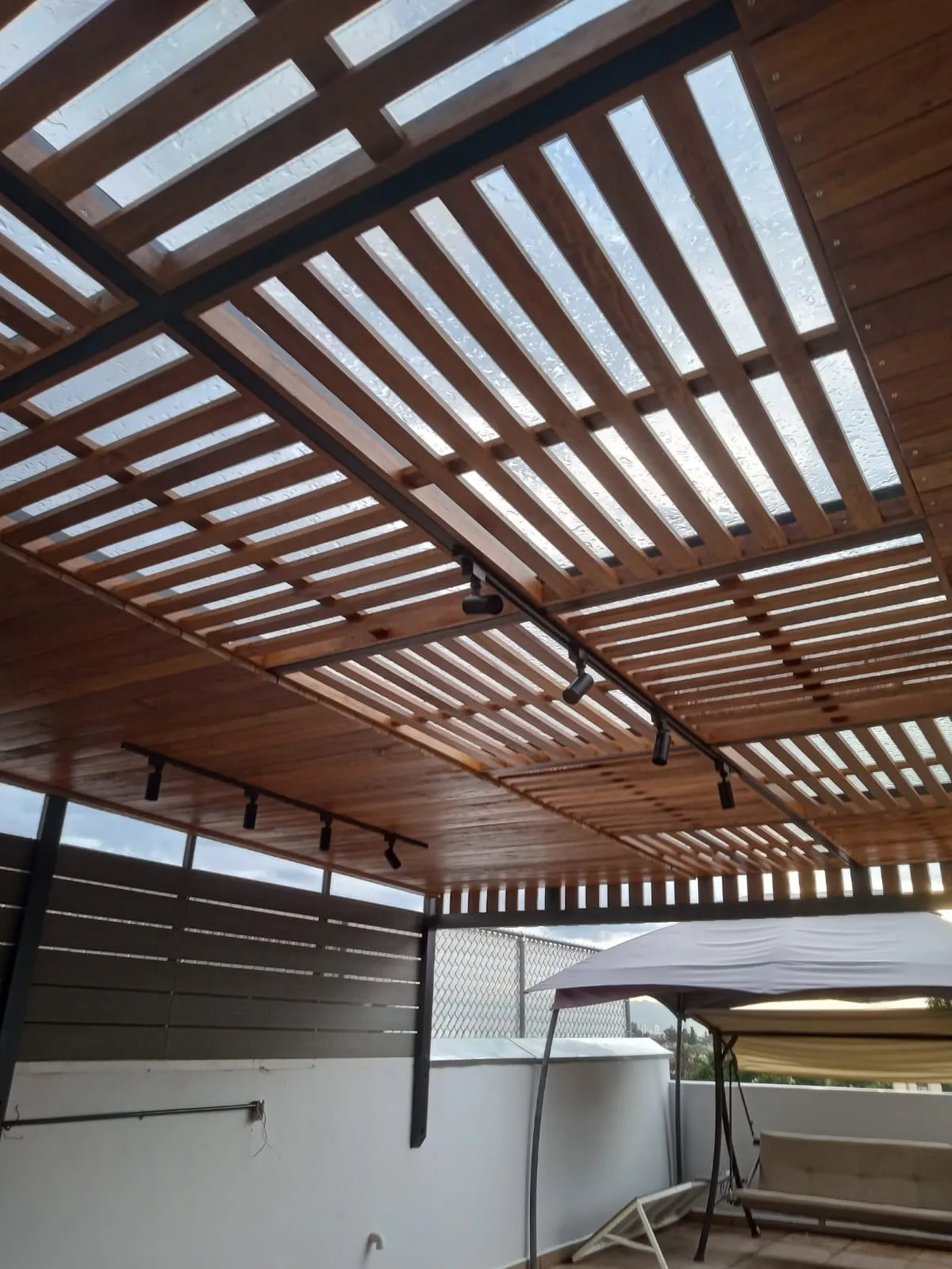 Techado de cristal con celosía de madera e iluminación de rieles en terraza