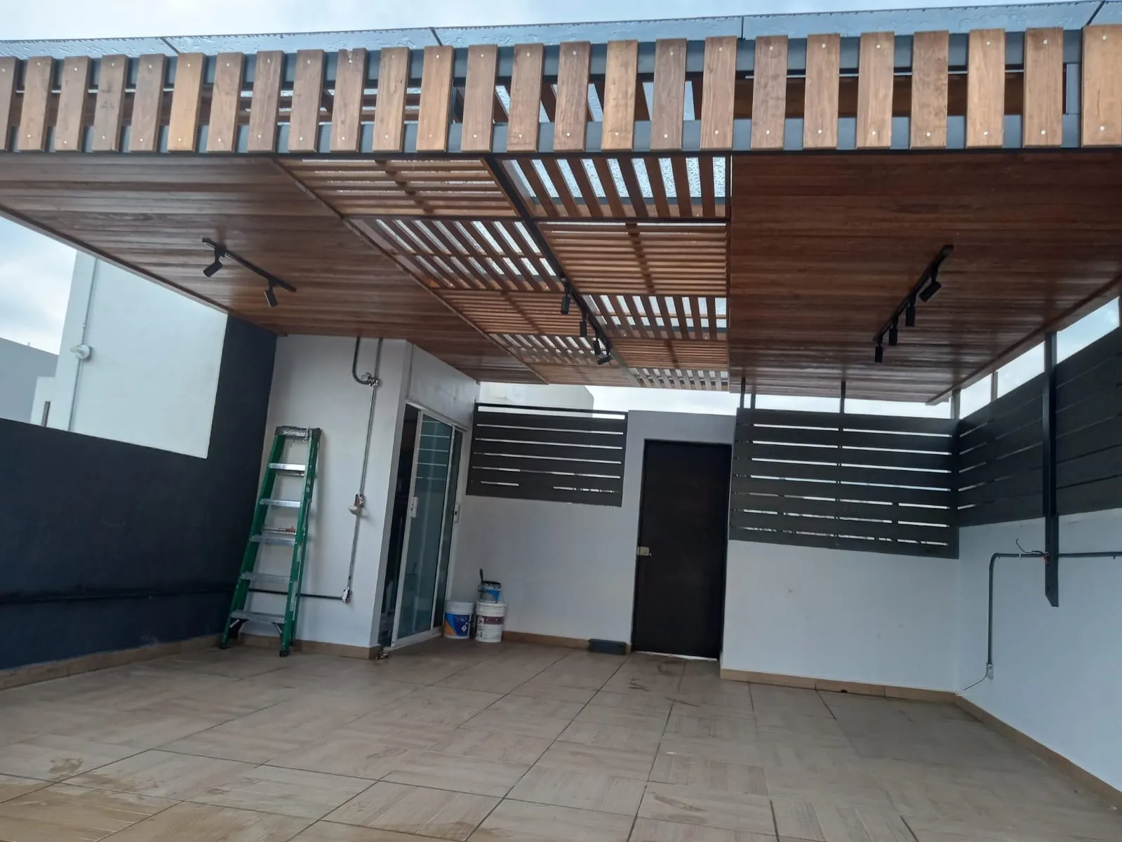 Techado de madera y cristal con lámparas de riel sobre patio con piso porcelánico