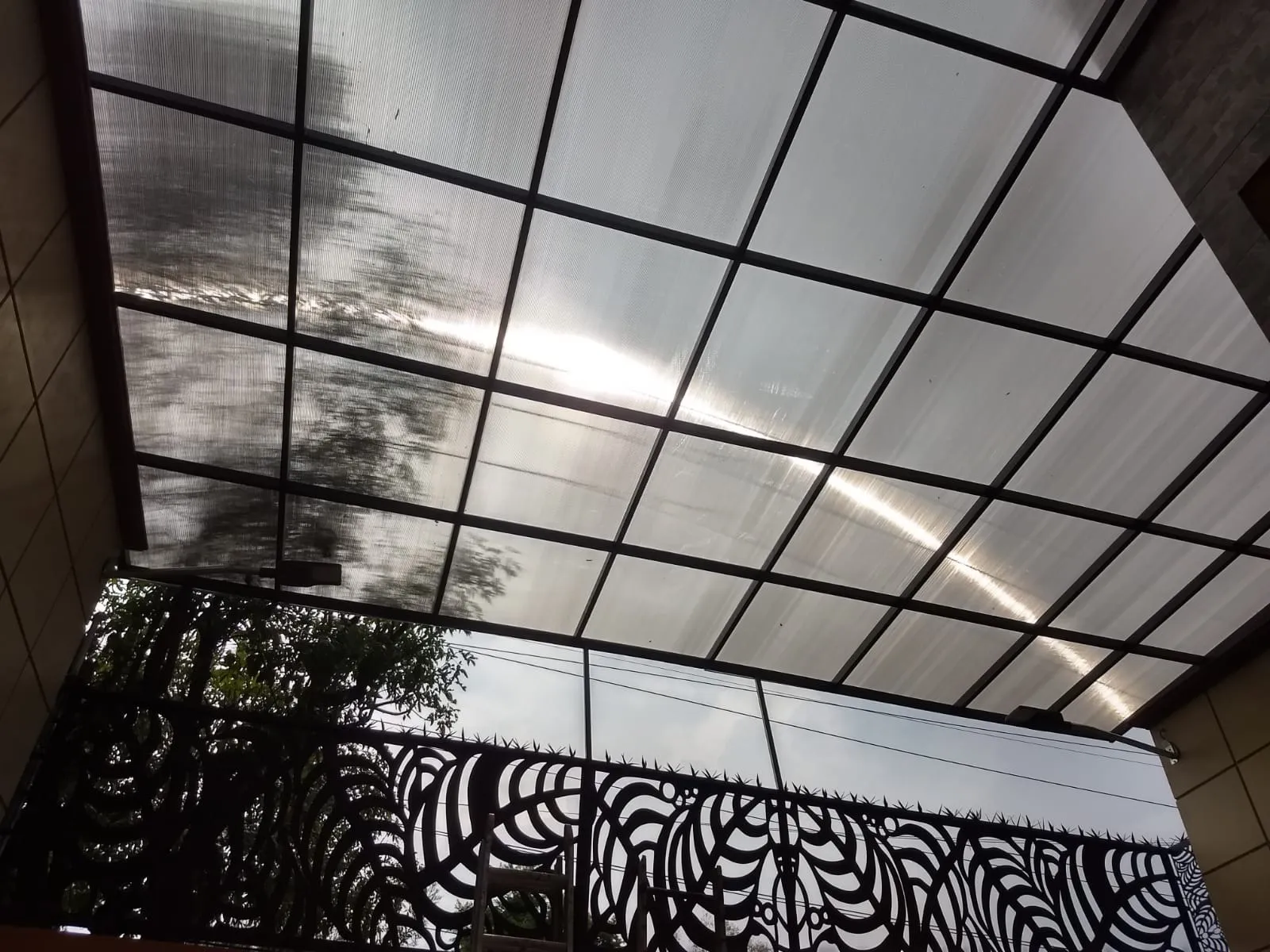 Techo de policarbonato con estructura de acero negro sobre terraza con barandal artístico