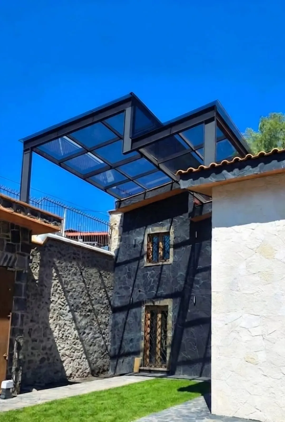 Techado en zeta de estructura metálica y cristal sobre el patio de una casa de piedra